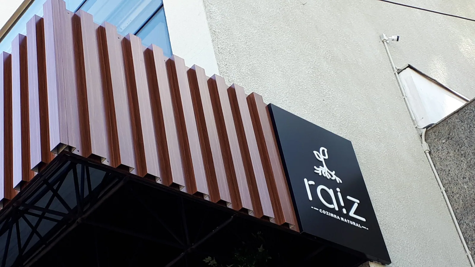 Raiz — Fachada com revestimento vertical e letreiro aplicado